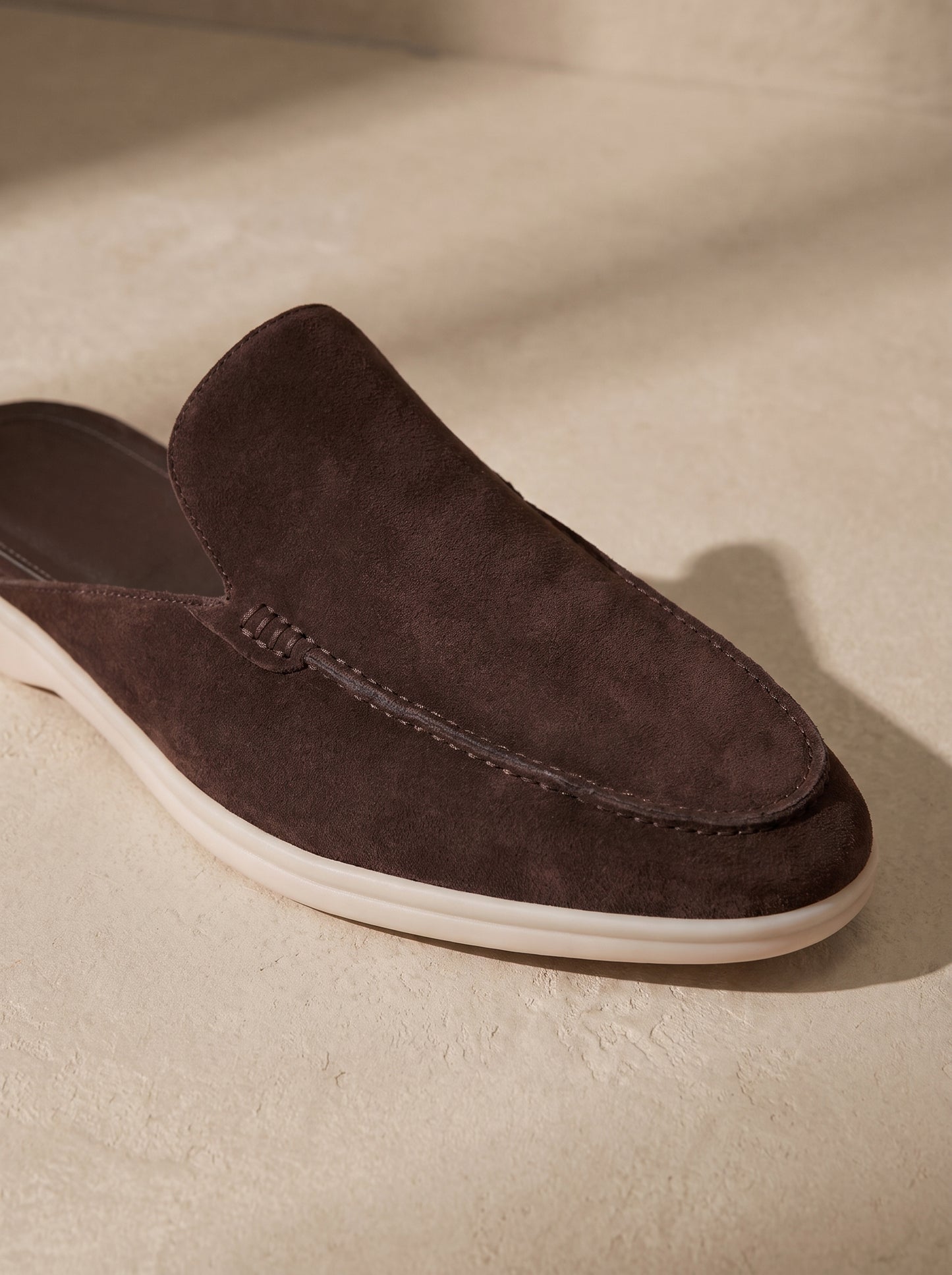 Mocasín mule de ante marrón con diseño tipo mocasín y suela blanca.