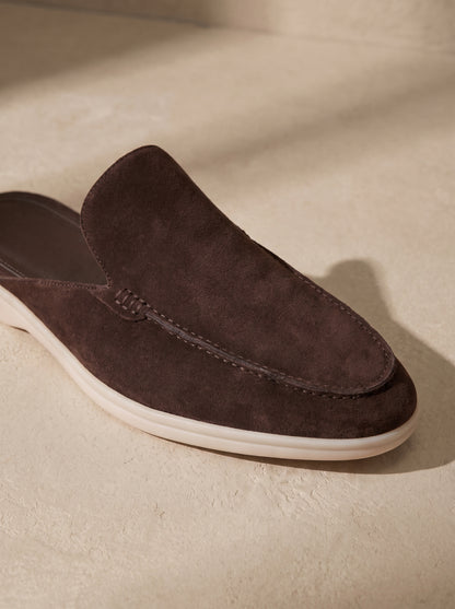 Mocasín mule de ante marrón con diseño tipo mocasín y suela blanca.