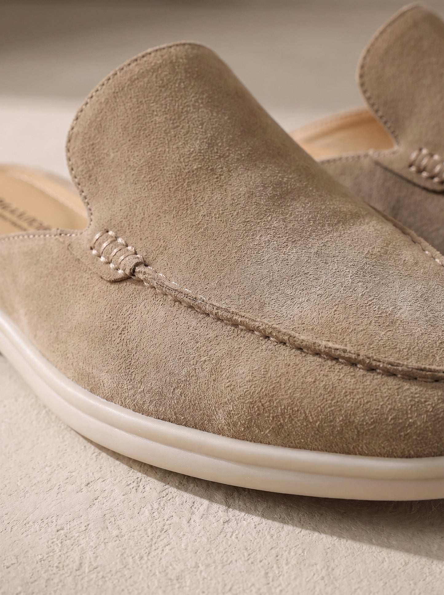 Mocasín mule de ante beige claro con costura en forma de cordón y suela blanca.