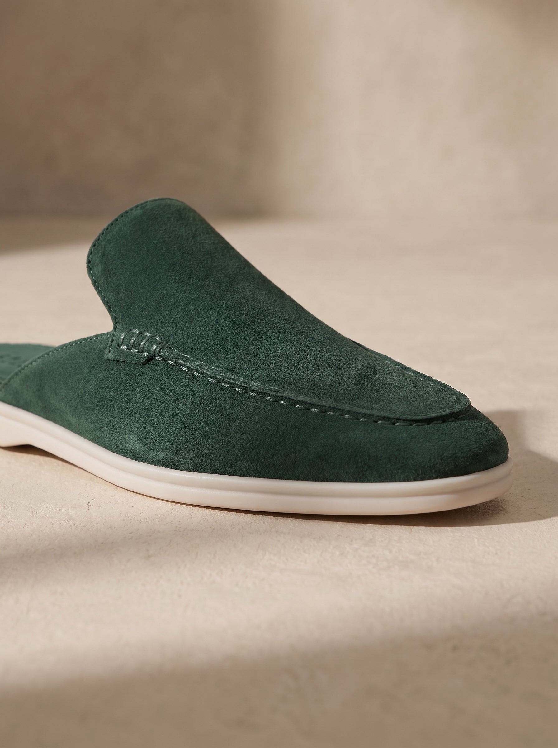 Mocasín mule de ante verde oscuro con abertura y suela blanca.