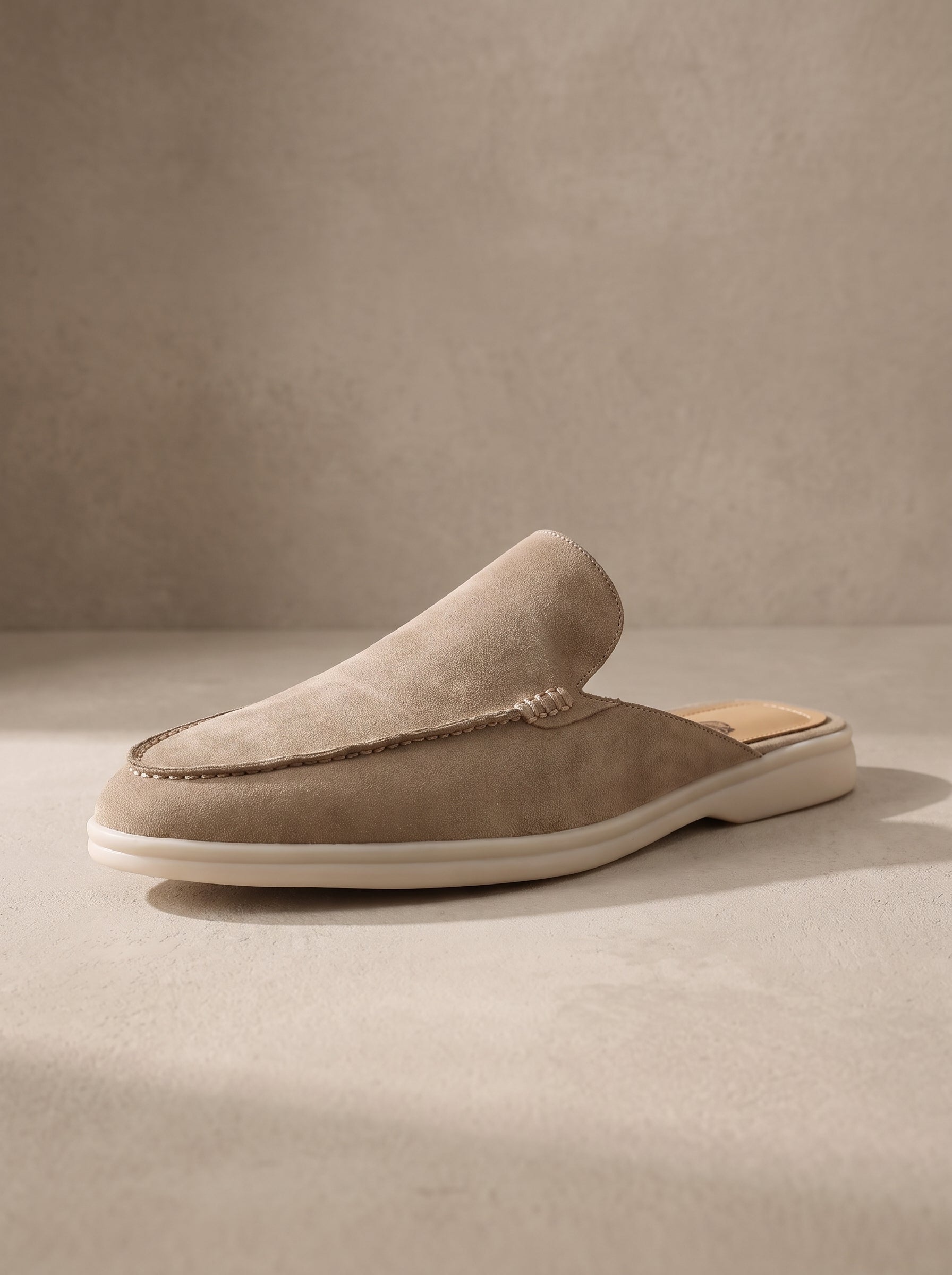 Mocasín mule de ante beige con costuras y suela blanca.