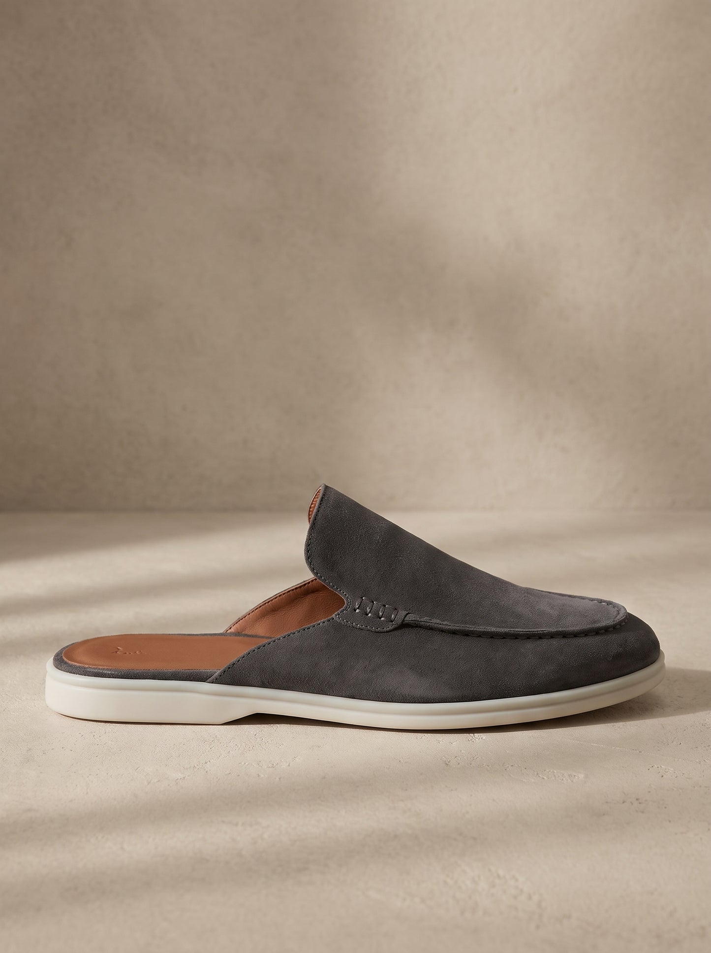 Mocasín mule de ante gris oscuro, sin cierre, con suela blanca y plantilla visible.
