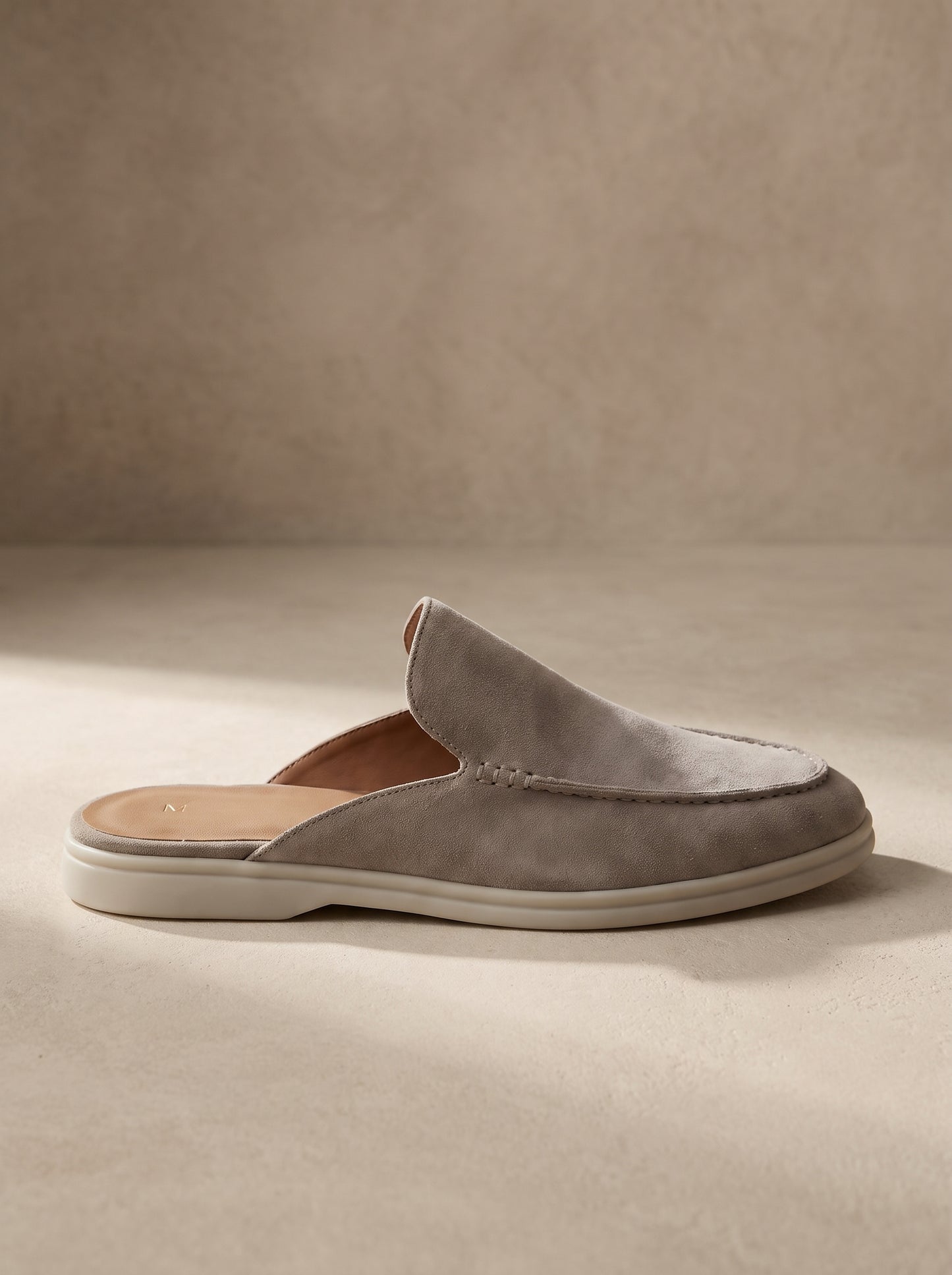 Mocasín mule de ante gris, diseño slip-on con suela blanca y pala ancha.