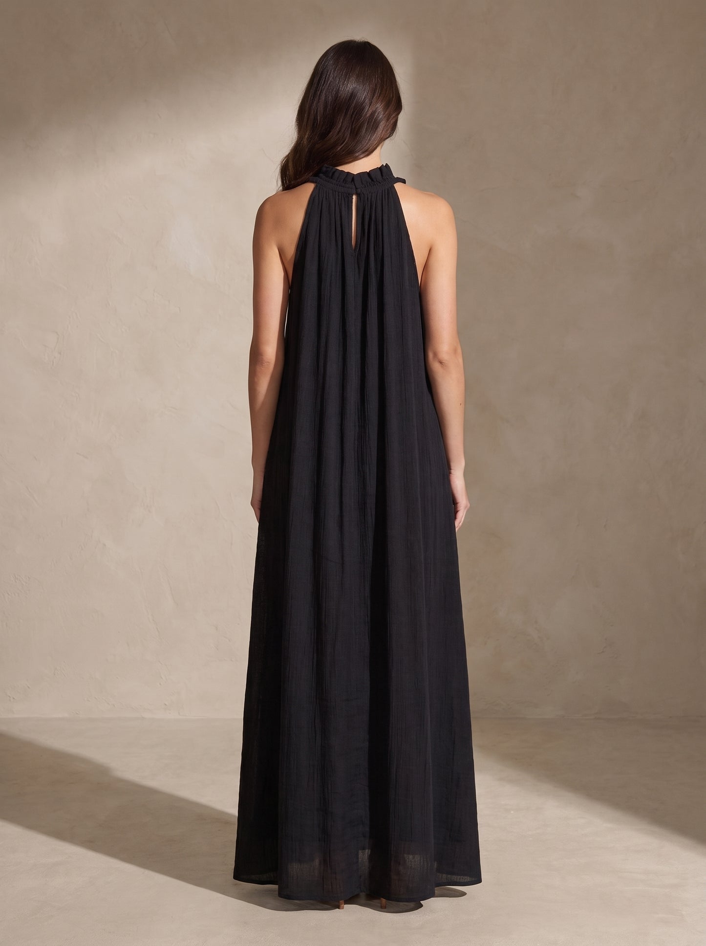 Vestido largo negro visto por detrás, tirantes halter con pliegues y caída suelta