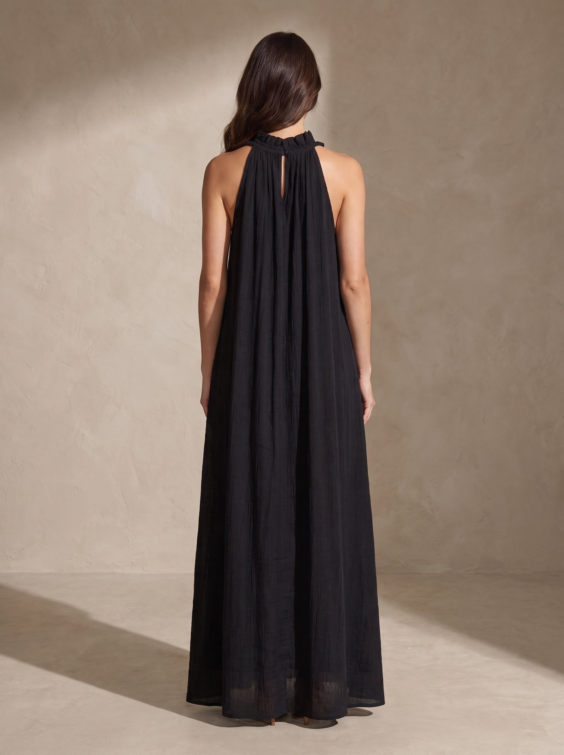Vestido largo negro visto por detrás, tirantes halter con pliegues y caída suelta