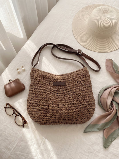 Bolso tejido marrón con asa de cuero marrón, etiqueta frontal y correa ajustable