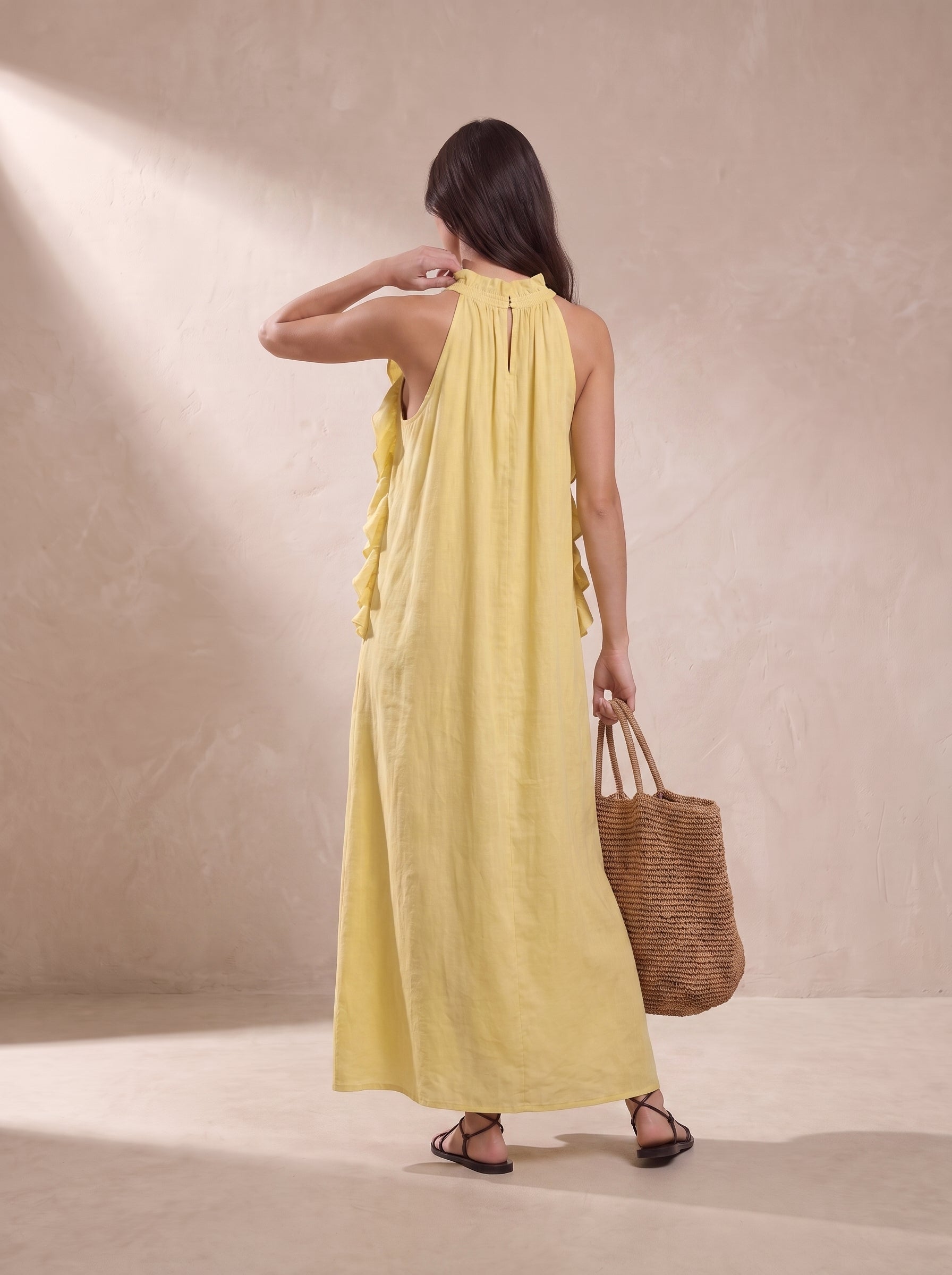 Vestido largo amarillo visto por detrás, tirantes halter con volantes y falda suelta