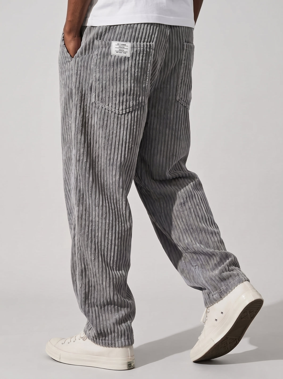 Pantalón de pana relajado gris oscuro, bolsillo trasero y pinzas visibles en la cintura.