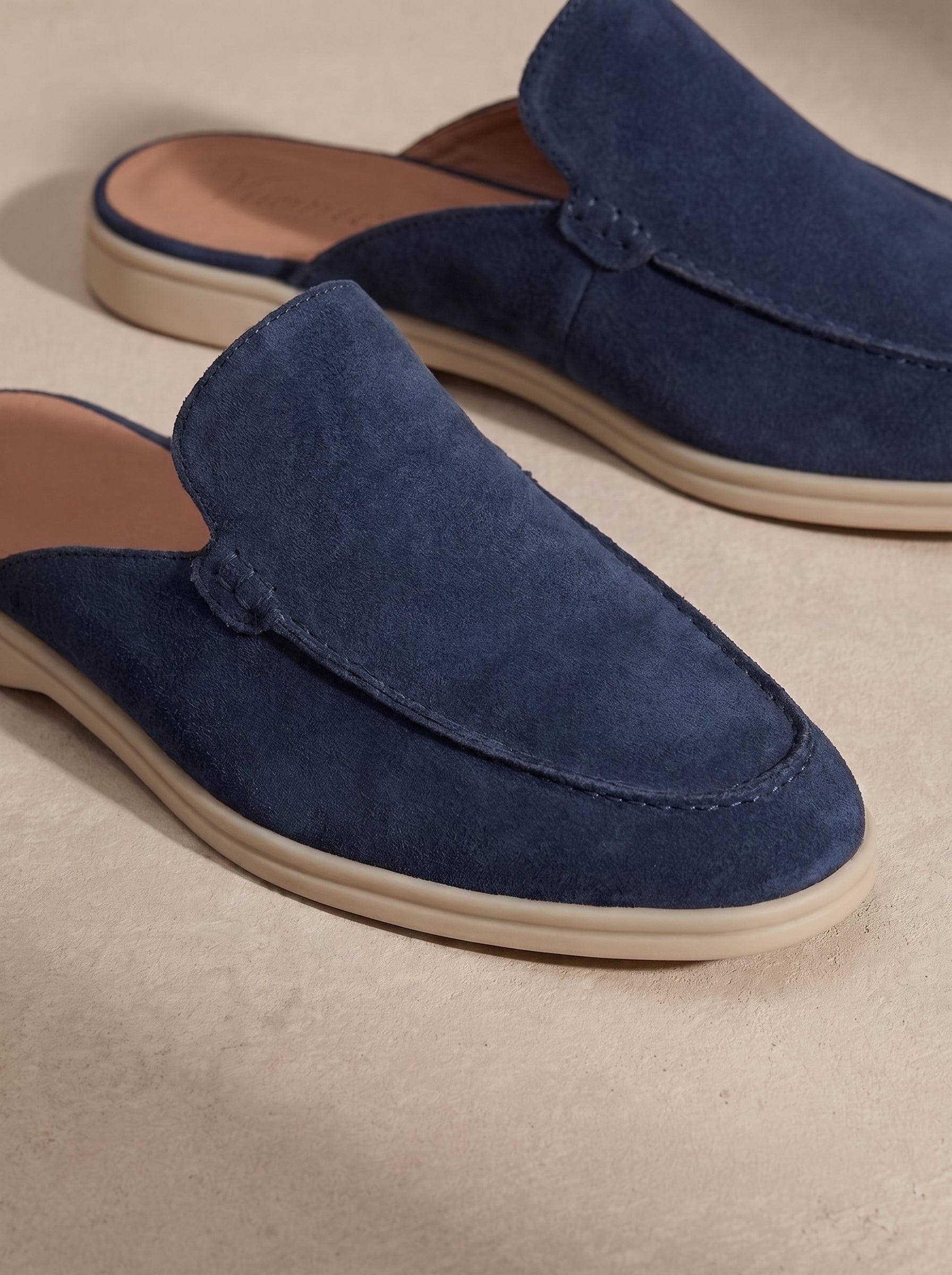 Mocasín mule de ante azul con costuras decorativas y suela beige.