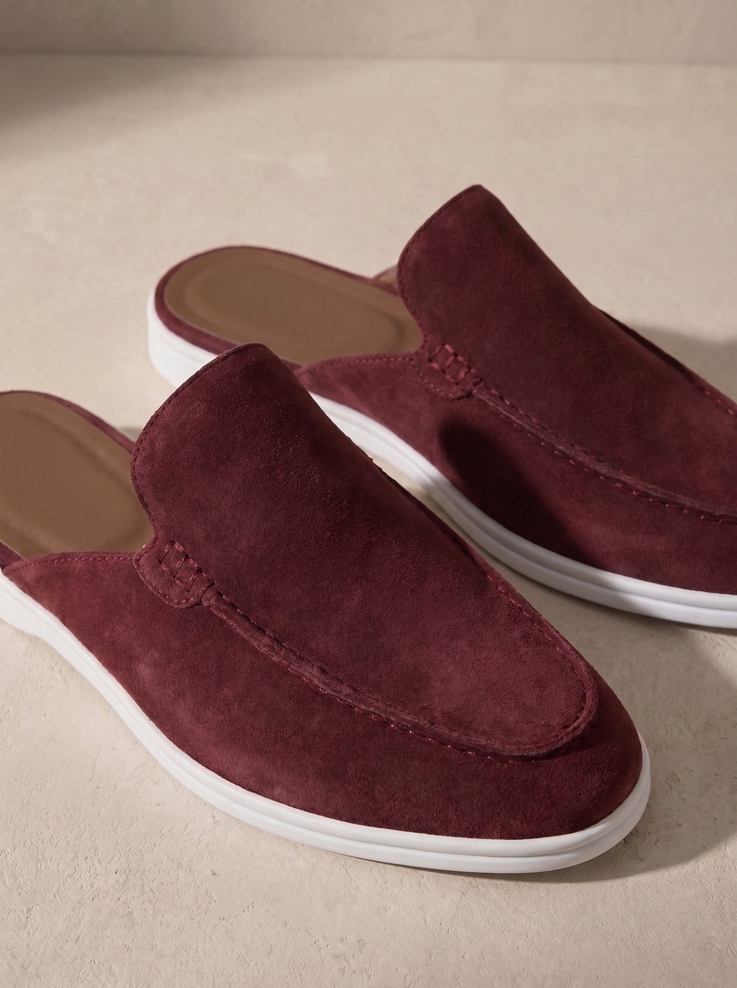 Mocasín mule de ante burdeos, perfil con suela blanca y acabado mate.